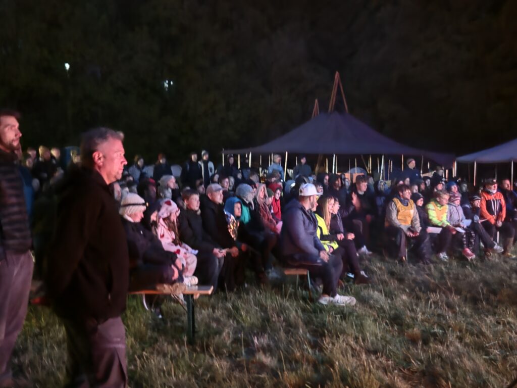 Teilnehmende und Helfende sitzen abends gemeinsam auf der Wiese und schauen zu