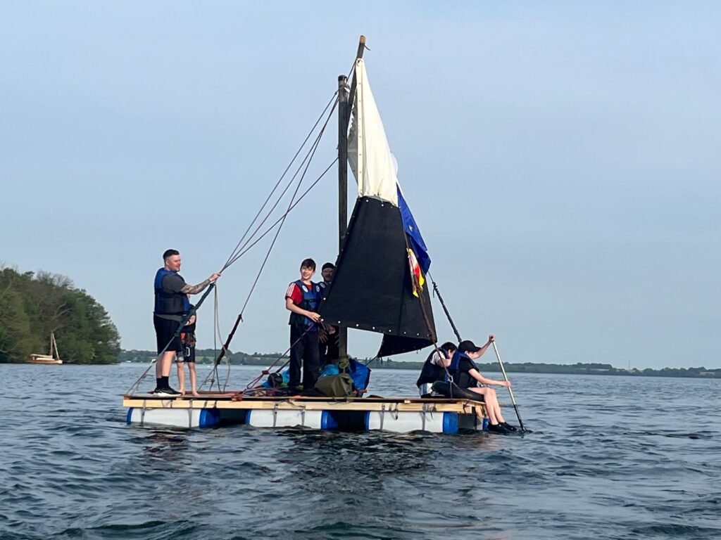 Ein Team auf einem selbstgebauten Floß mit Segel auf dem Wasser